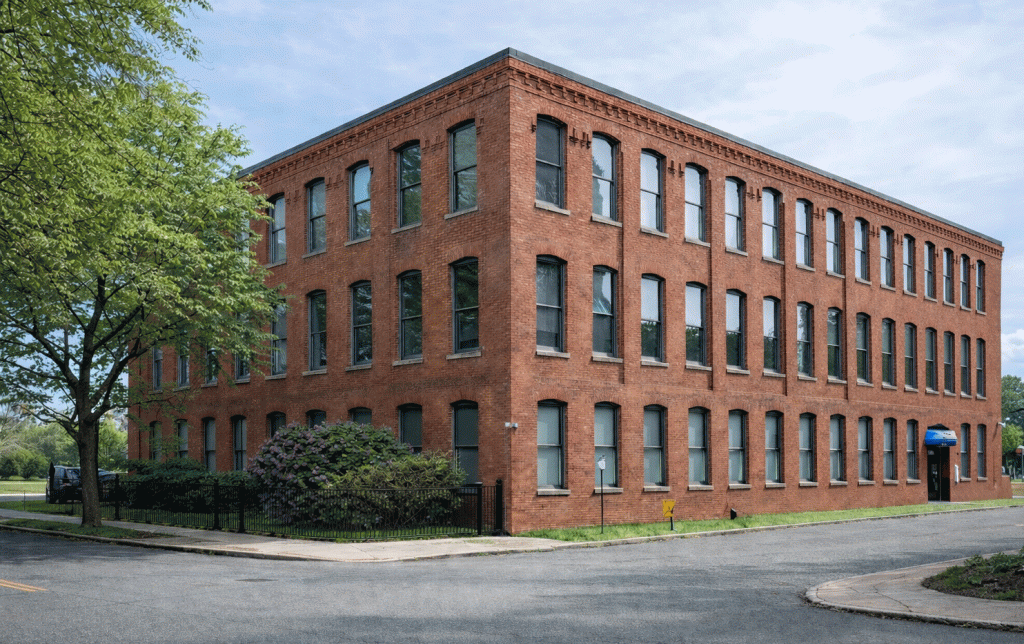 Three-story red brick building with rows of arched windows on a corner lot in Hartford, CT