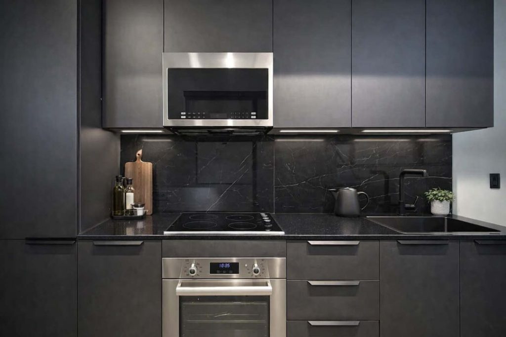 Modern dark kitchen with stainless steel microwave and oven, black marble backsplash, and matte cabinetry